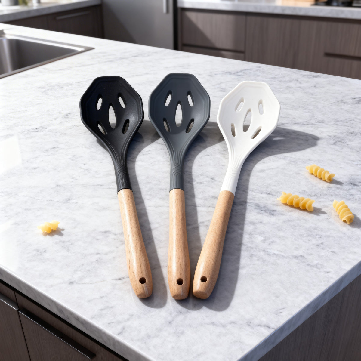 Trendy Shop set of three silicone slotted spoons in black, grey, and white with wooden handles on a marble counter.