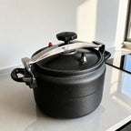 Vallena stainless steel and black non-stick pressure cooker with a secure locking handle on a kitchen countertop.